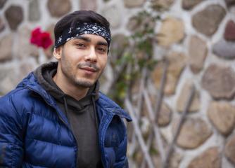 Se framtiden - leende mörkhårig kille i blå jacka står framför en stenvägg utomhus