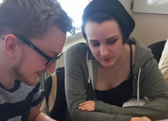 En tjej och en kille sitter och jobbar tillsammans med en bok