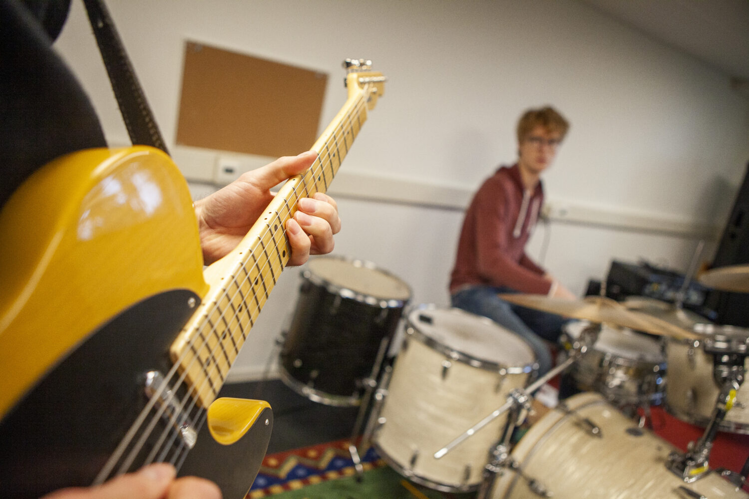En elgitarr och i bakgrunden en ung man som spelar trummor