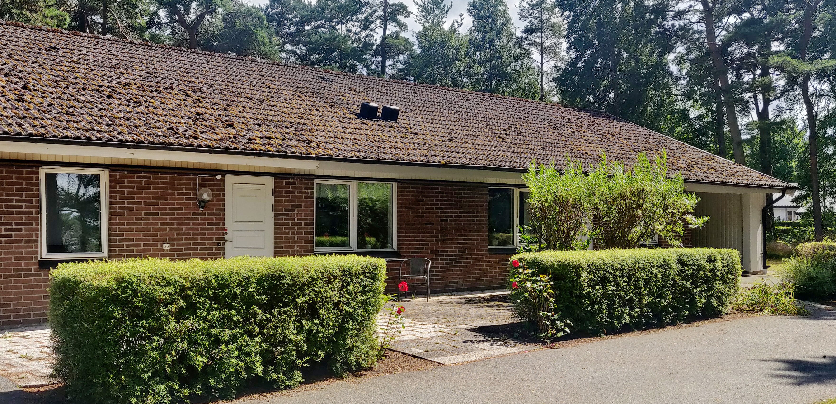 Rött tegelhus med grönskande häck framför del av huset.