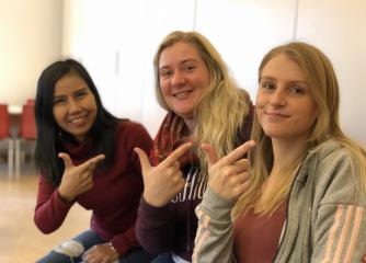 Tre unga kvinnor gör ett tecken på teckenspråk