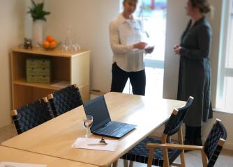 Ett konferensbord och i bakgrunden står två personer 