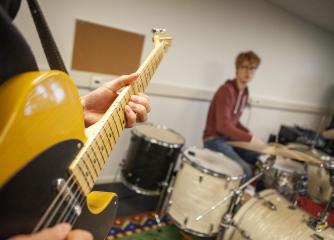 En elgitarr och i bakgrunden en ung man som spelar trummor