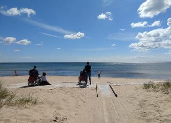 Några personer på en strand tittar ut mot havet och blå himmel med lätta moln