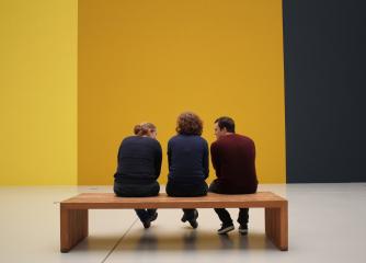 Tre personer på en bänk framför en gul vägg