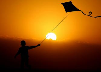 Ett barn som håller en drake, i bakgrunden en solnedgång.